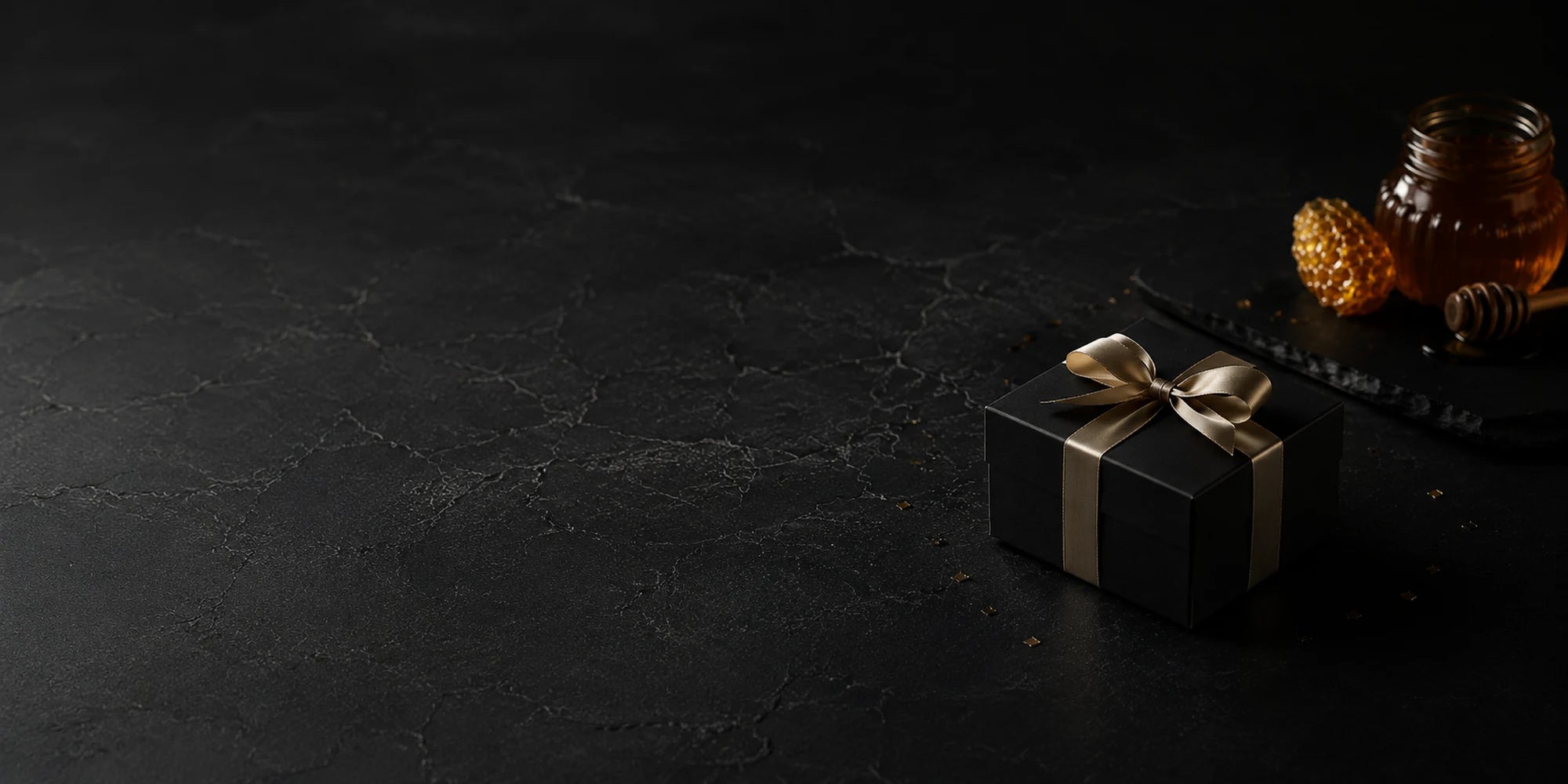 A wrapped gift beside honey on a dark stone surface